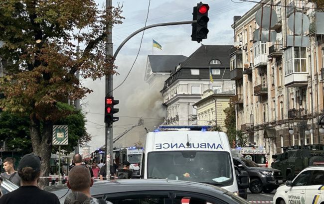 На міській вулиці стоять машини швидкої допомоги, у небі над будинками видно густий дим